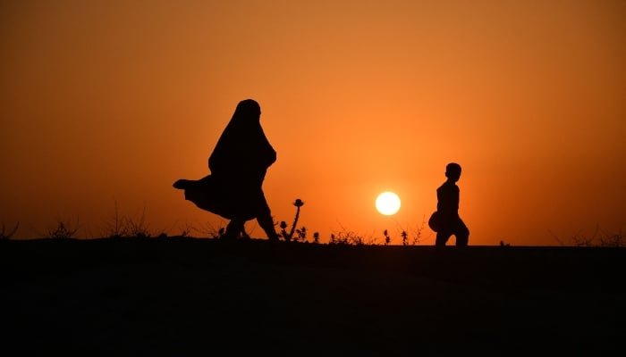 An Afghan woman and a boy walk along a hillside during sunset on the outskirts of Mazar-e-Sharif on June 4, 2025. — AFP
