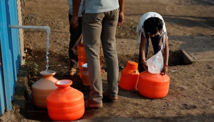 A girl covers a pot filled with water with a plastic sheet to protect it from dust next to a water ATM machine in Solapur, India, March 3, 2025. — Reuters